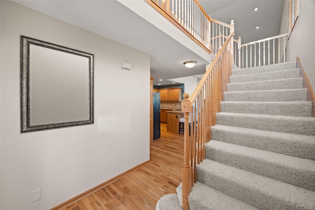 stairs featuring recessed lighting, wood finished floors, baseboards, and a towering ceiling