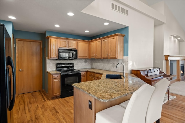 kitchen with light wood finished floors, visible vents, a peninsula, black appliances, and a sink