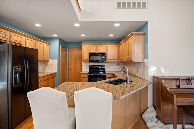 kitchen with visible vents, black appliances, a sink, a peninsula, and light stone countertops