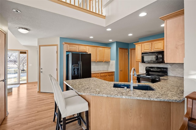 kitchen featuring light wood-type flooring, black appliances, light brown cabinetry, light stone counters, and a peninsula