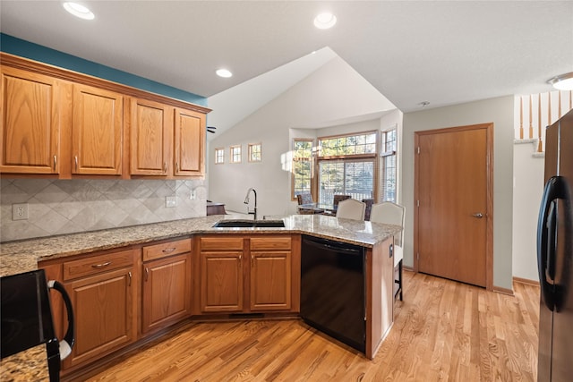 kitchen with light wood finished floors, decorative backsplash, a peninsula, black appliances, and a sink