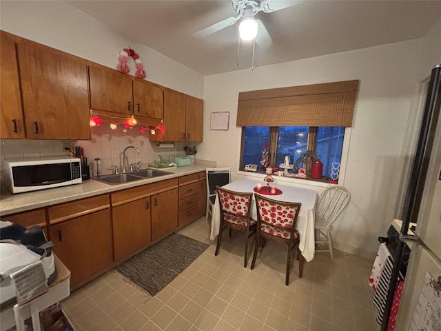 kitchen featuring brown cabinetry, white microwave, a sink, light countertops, and backsplash