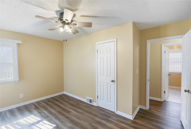 unfurnished bedroom featuring a ceiling fan, baseboards, visible vents, dark wood-style flooring, and a textured ceiling