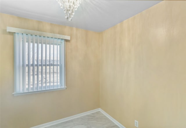 spare room with baseboards, marble finish floor, and an inviting chandelier