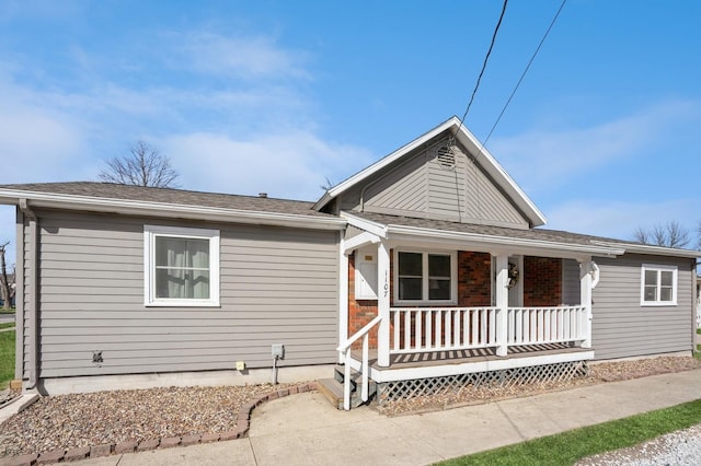 ranch-style home featuring brick siding, covered porch, and a shingled roof