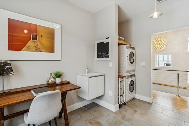 clothes washing area with baseboards, stacked washer and clothes dryer, and laundry area