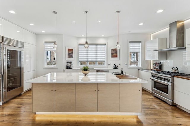 kitchen featuring light wood finished floors, light countertops, wall chimney range hood, modern cabinets, and premium appliances