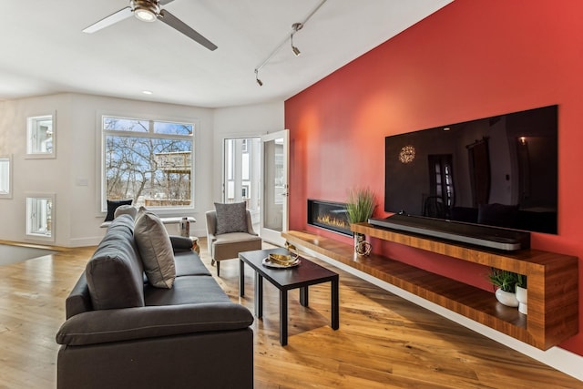 living area featuring wood finished floors, a ceiling fan, a glass covered fireplace, and rail lighting