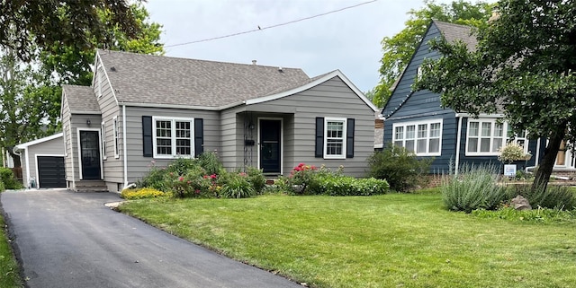 view of front of property featuring entry steps, a shingled roof, a detached garage, and a front yard