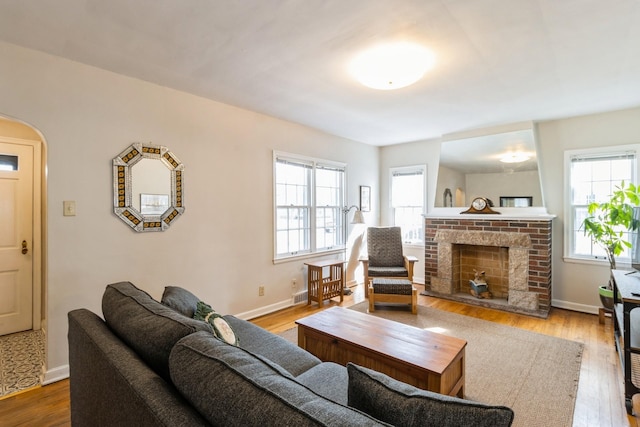 living area featuring arched walkways, a fireplace, baseboards, and wood finished floors