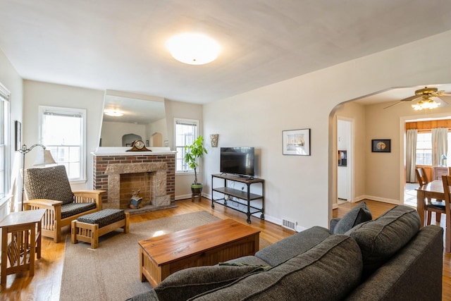 living room featuring visible vents, wood finished floors, arched walkways, a fireplace, and baseboards