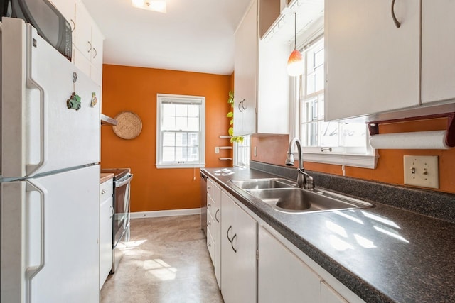 kitchen with baseboards, stainless steel range with electric cooktop, freestanding refrigerator, white cabinetry, and a sink