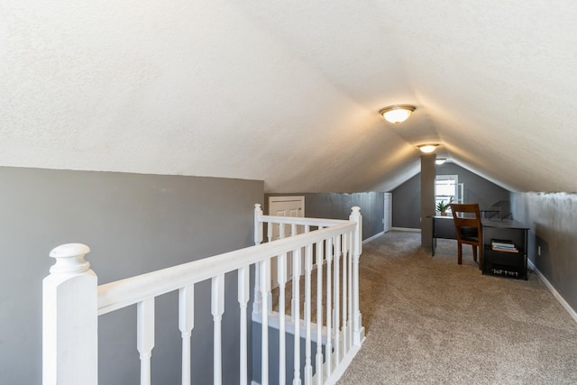 interior space featuring baseboards, vaulted ceiling, a textured ceiling, carpet flooring, and an upstairs landing