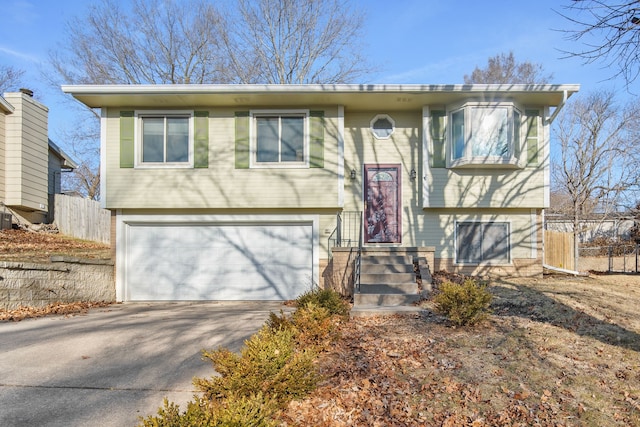 split foyer home with an attached garage, concrete driveway, and fence