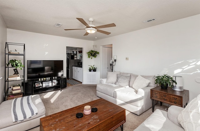 carpeted living room featuring a ceiling fan, visible vents, and a textured ceiling