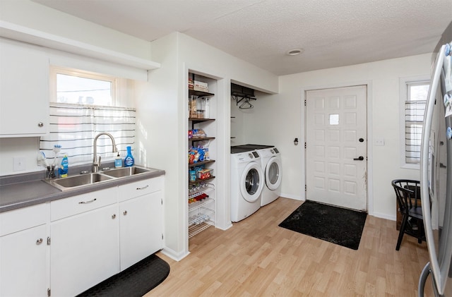 laundry area featuring baseboards, a sink, light wood-style floors, a textured ceiling, and washer and clothes dryer