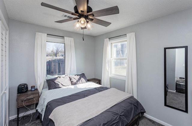 carpeted bedroom with multiple windows, a ceiling fan, baseboards, and a textured ceiling