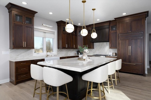 kitchen with light wood-type flooring, a breakfast bar, tasteful backsplash, a kitchen island, and paneled built in fridge