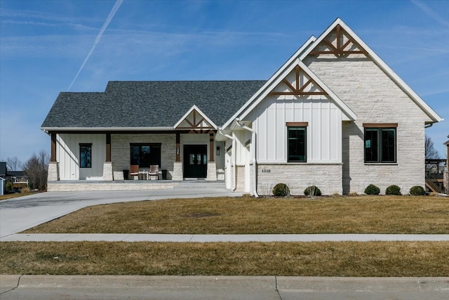 modern inspired farmhouse featuring board and batten siding, a shingled roof, a porch, a front yard, and stone siding