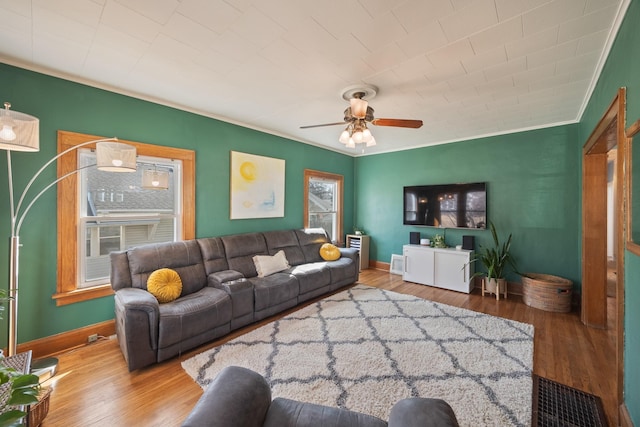 living area featuring a ceiling fan, wood finished floors, baseboards, and ornamental molding