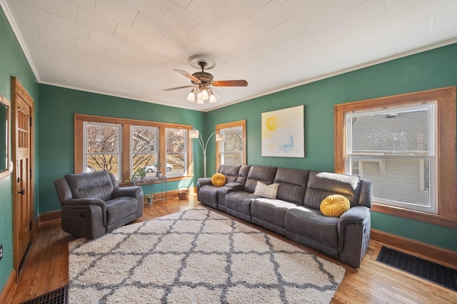 living room with visible vents, wood finished floors, crown molding, baseboards, and ceiling fan