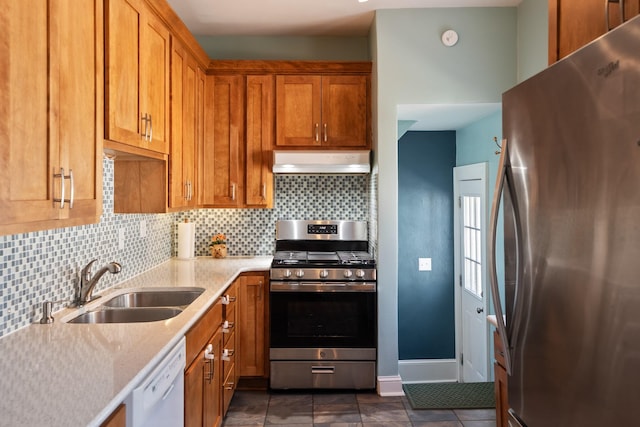 kitchen with brown cabinetry, a sink, under cabinet range hood, appliances with stainless steel finishes, and tasteful backsplash