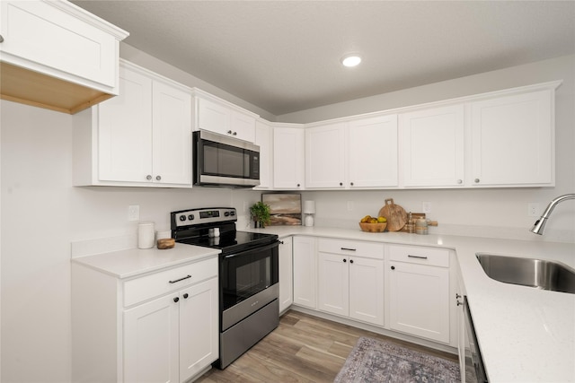 1506 E Girard Ave, Indianola, IA 50125 - kitchen with appliances with stainless steel finishes, a sink, light wood-style flooring, white cabinetry, and recessed lighting