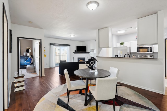 dining space featuring baseboards, a lit fireplace, and dark wood-style flooring