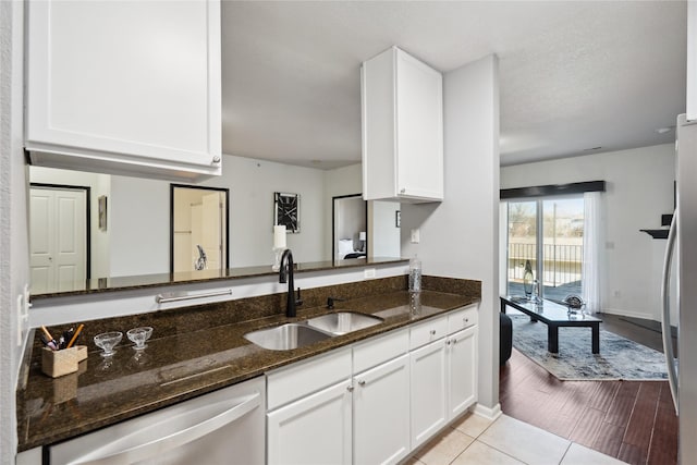 kitchen with white cabinetry, stainless steel dishwasher, dark stone counters, and a sink