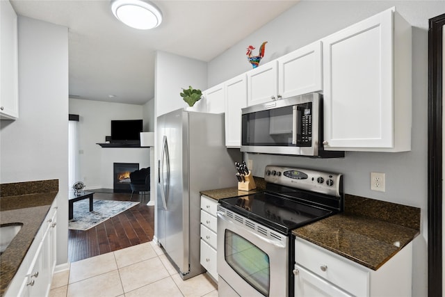 kitchen featuring dark stone countertops, white cabinets, light tile patterned floors, and stainless steel appliances