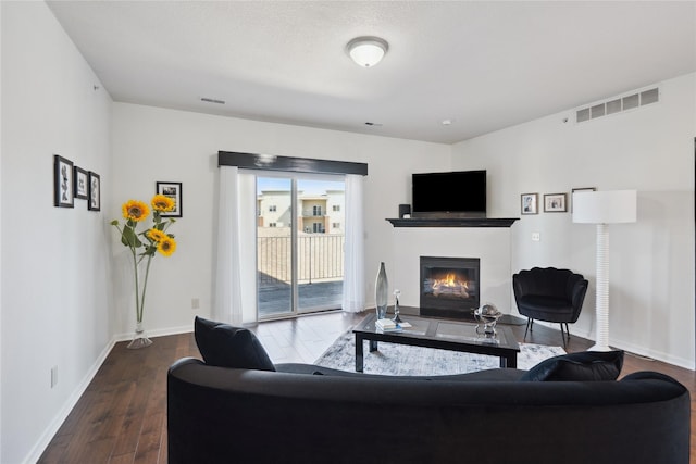 living area featuring visible vents, wood finished floors, baseboards, and a glass covered fireplace