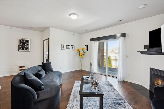 living area with visible vents, baseboards, a glass covered fireplace, and dark wood-style flooring