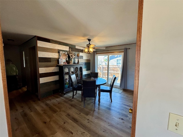 dining room featuring wooden walls, a textured ceiling, ceiling fan, and wood finished floors