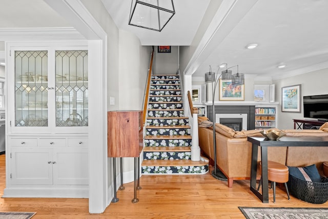 stairway with a glass covered fireplace, a wainscoted wall, wood finished floors, and crown molding