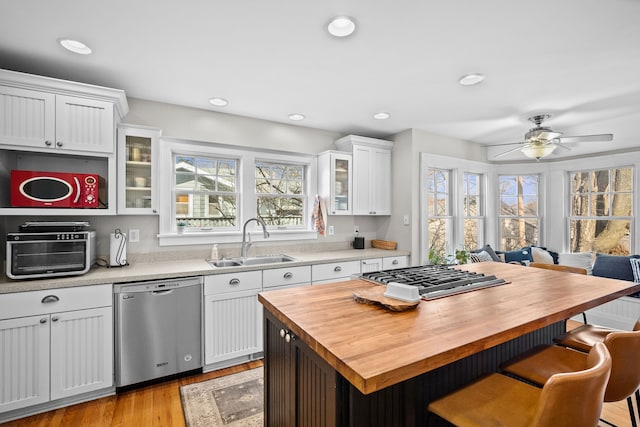 kitchen featuring wooden counters, a sink, stainless steel appliances, glass insert cabinets, and a kitchen bar