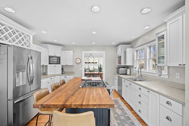 kitchen with a breakfast bar, a sink, stainless steel appliances, white cabinets, and wood counters