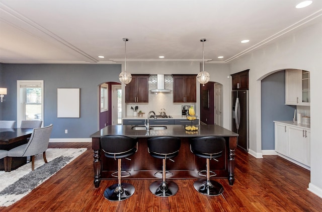 kitchen with a kitchen bar, a sink, arched walkways, stainless steel fridge, and wall chimney exhaust hood