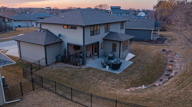 back of house at dusk featuring central air condition unit, a lawn, fence, a shingled roof, and a patio area