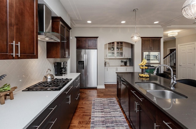 kitchen with a sink, decorative light fixtures, appliances with stainless steel finishes, wall chimney exhaust hood, and dark wood-style flooring