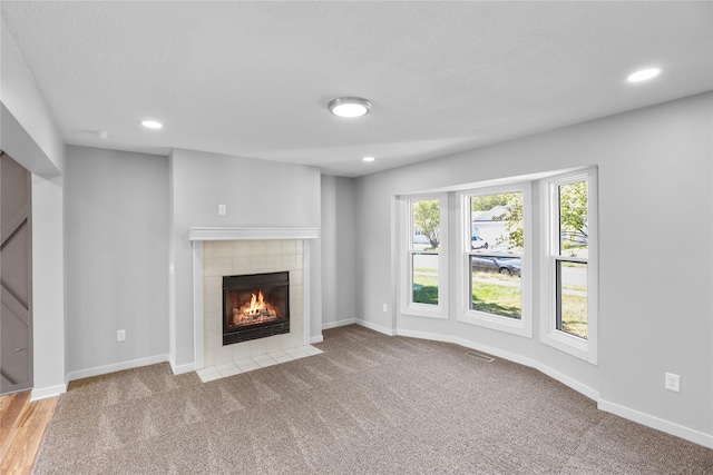 unfurnished living room with a tiled fireplace, baseboards, and visible vents