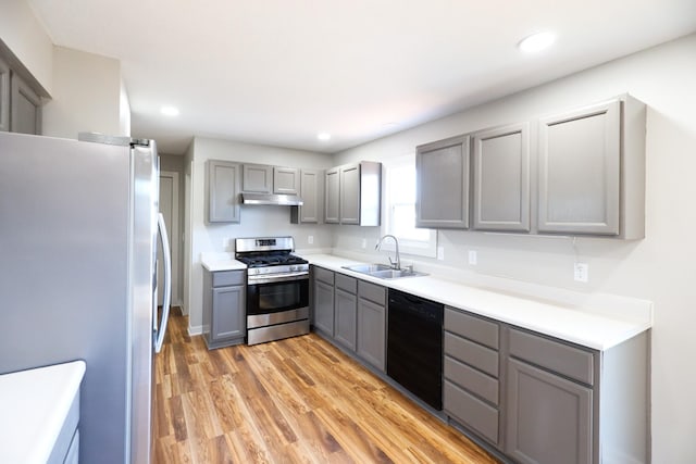 kitchen featuring light wood-style flooring, gray cabinets, a sink, under cabinet range hood, and appliances with stainless steel finishes