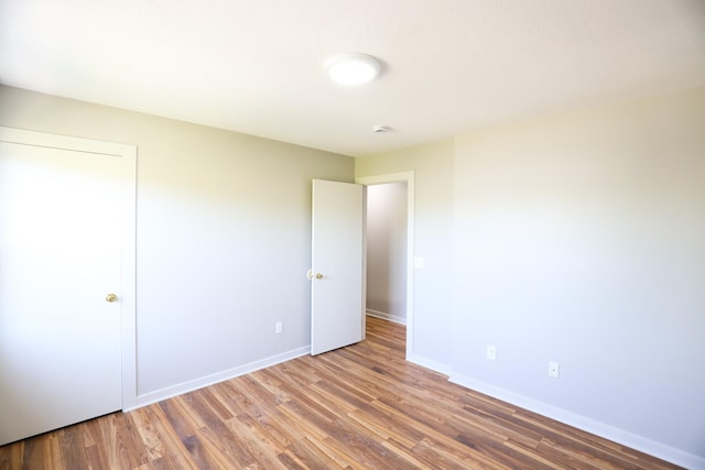 unfurnished bedroom featuring wood finished floors, baseboards, and a closet