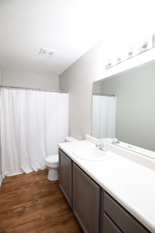 full bathroom featuring vanity, wood finished floors, visible vents, a textured ceiling, and toilet