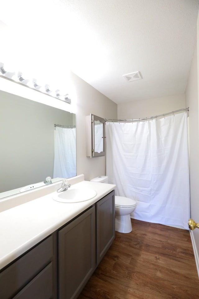 bathroom with visible vents, toilet, curtained shower, wood finished floors, and vanity