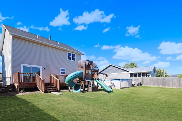 back of house with a deck, a playground, fence, a yard, and a fenced in pool