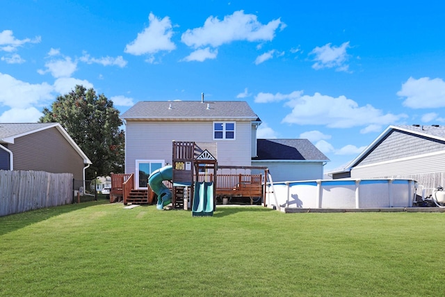 rear view of property with a lawn, an outdoor pool, a deck, and fence