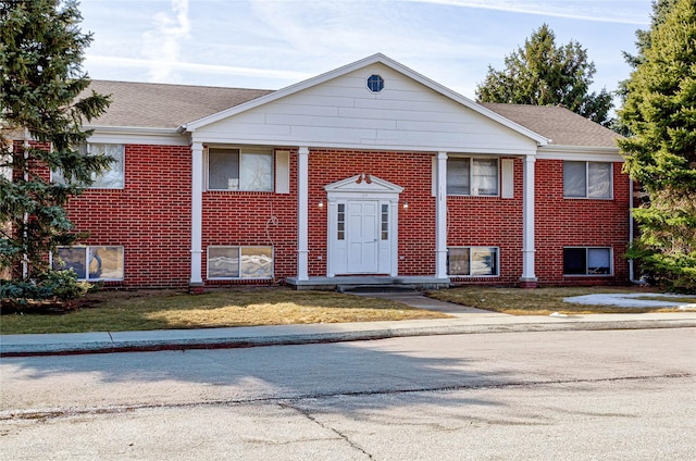 bi-level home with brick siding, a shingled roof, and a front lawn