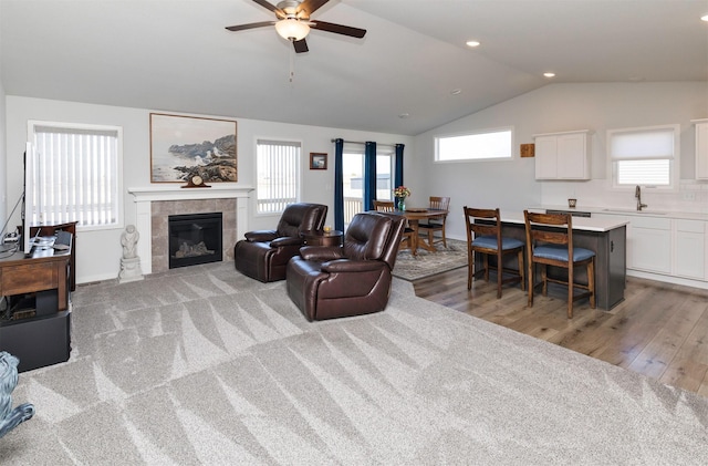 living room featuring a tiled fireplace, a healthy amount of sunlight, light wood-style flooring, and vaulted ceiling