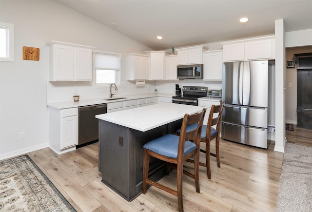 kitchen with a sink, a kitchen island, stainless steel appliances, white cabinets, and light countertops