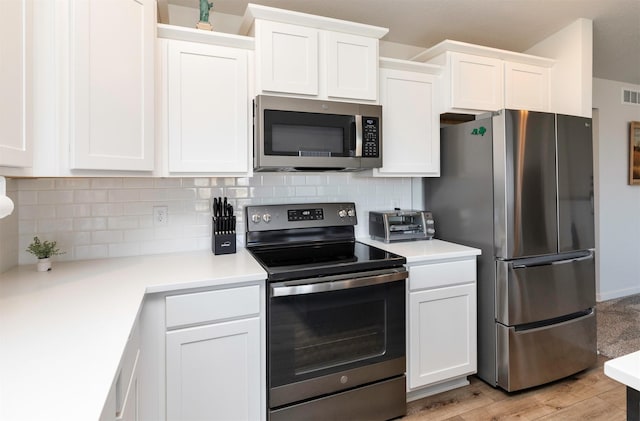 kitchen with visible vents, light wood-style flooring, stainless steel appliances, white cabinetry, and backsplash